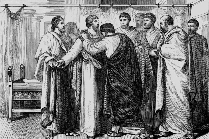 A man greeting another man with a kiss among a group of robed men