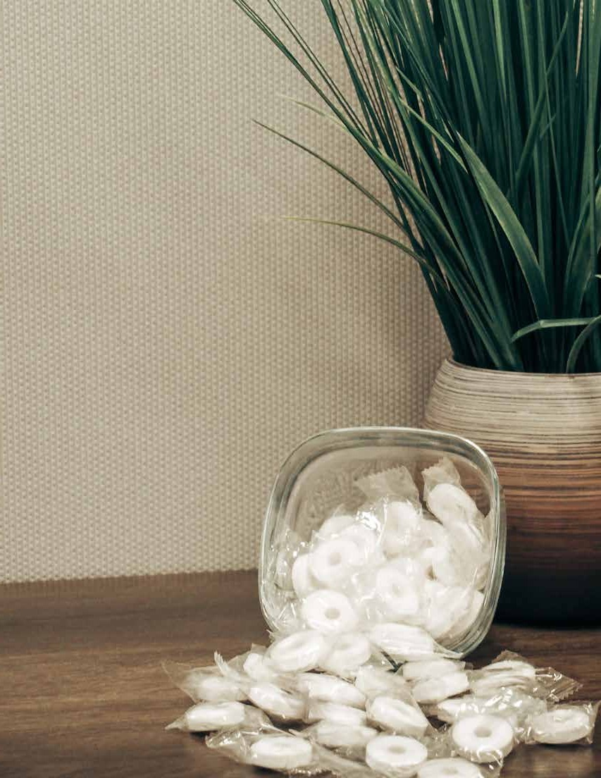 A glass jar spilling wrapped mints beside a potted plant