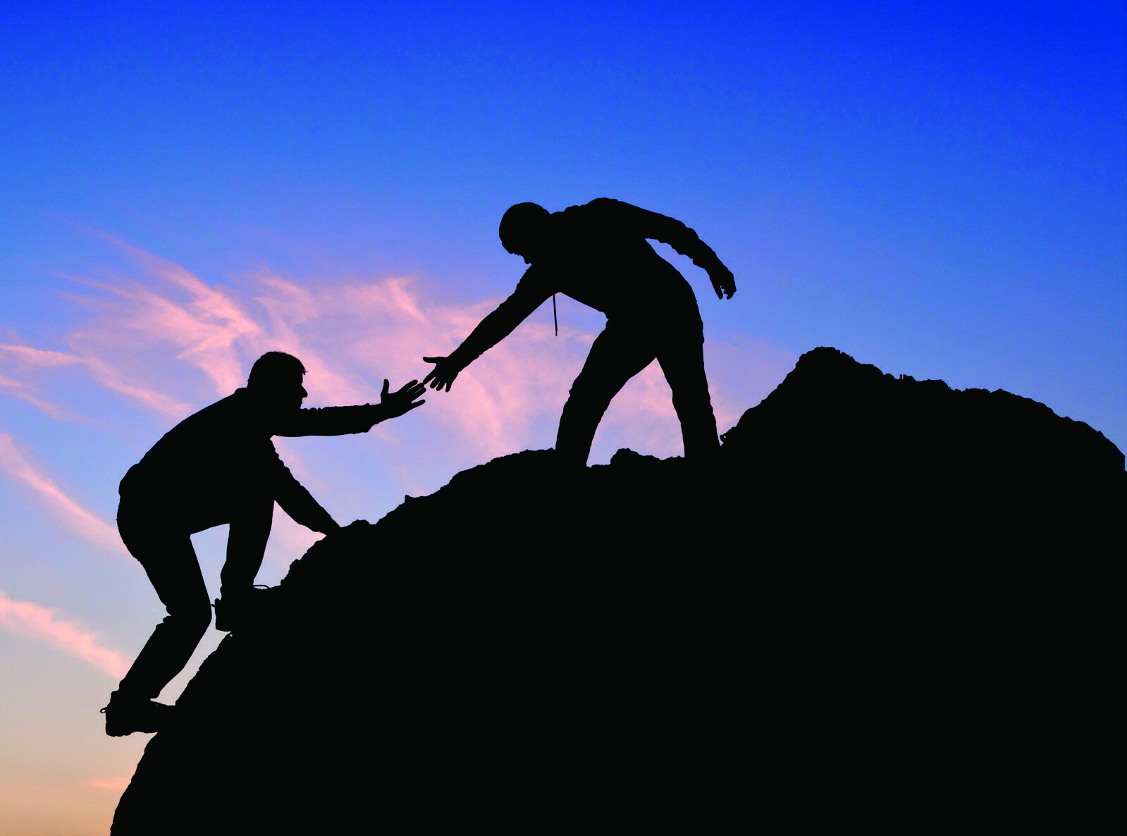 Two climbers helping each other up a steep ridge at dusk