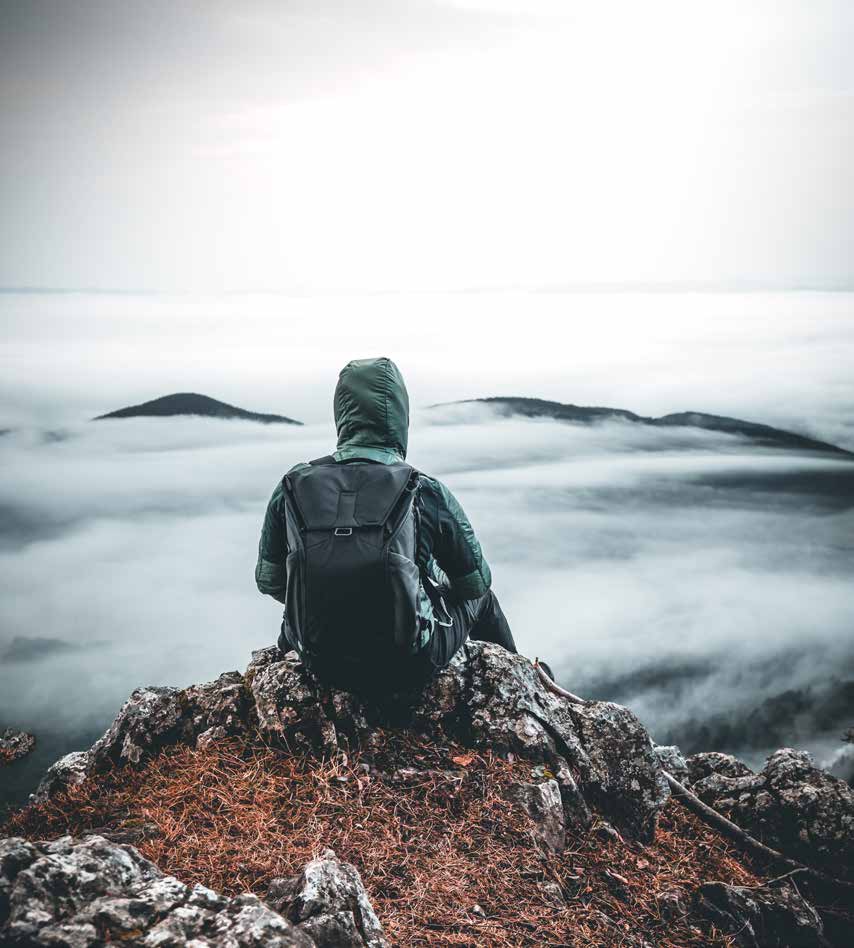 Solitary hooded person with a backpack seated above a misty landscape