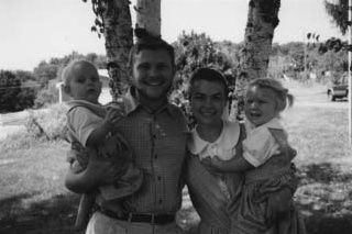 A man and woman standing outdoors, each holding a young child.