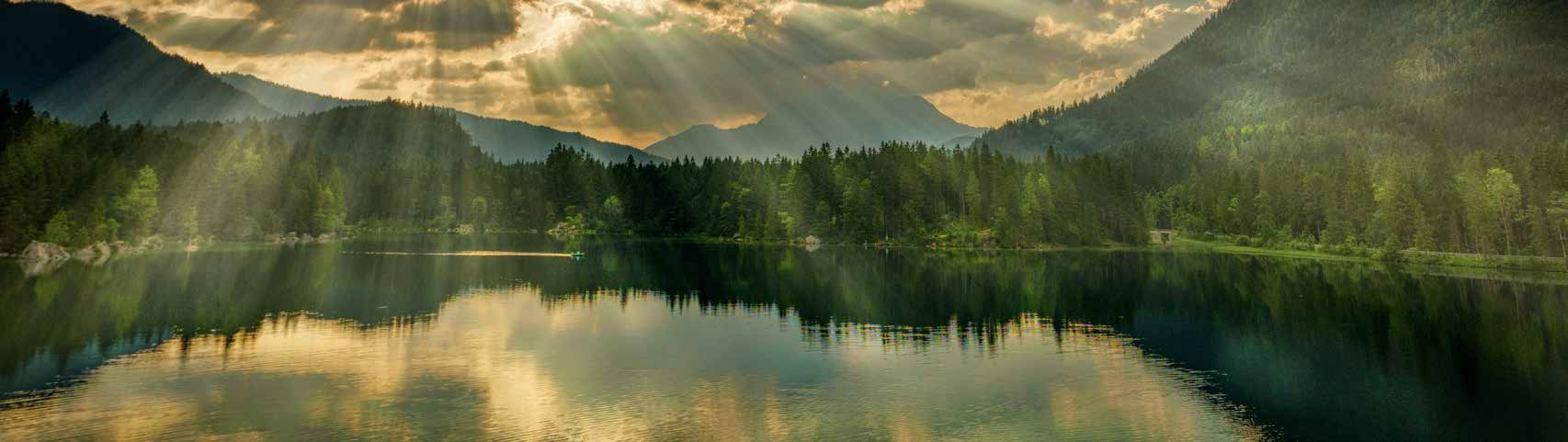 Sunbeams break through clouds over a forested mountain lake