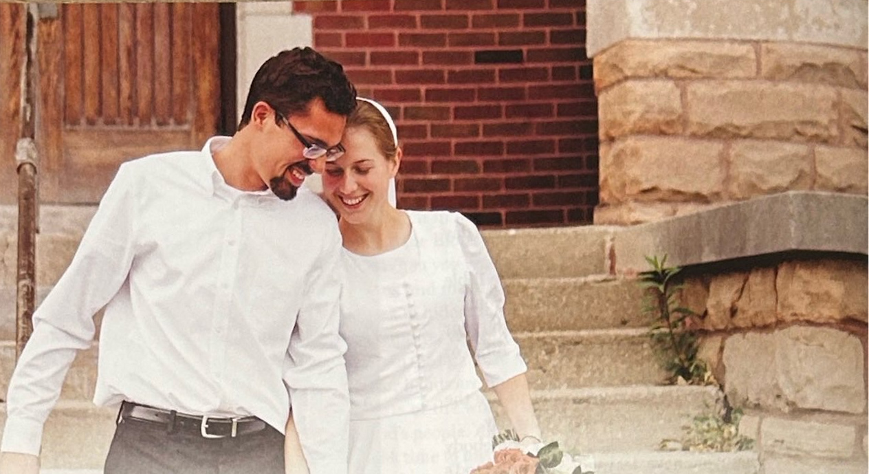 A bride and groom leaning their heads together outside a building.