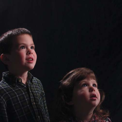A boy and girl looking upward against a dark background