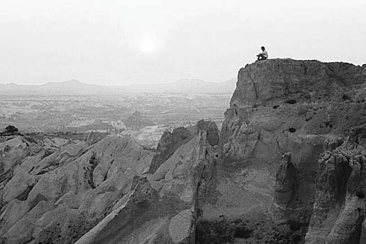 A solitary person sitting on the edge of a desert cliff
