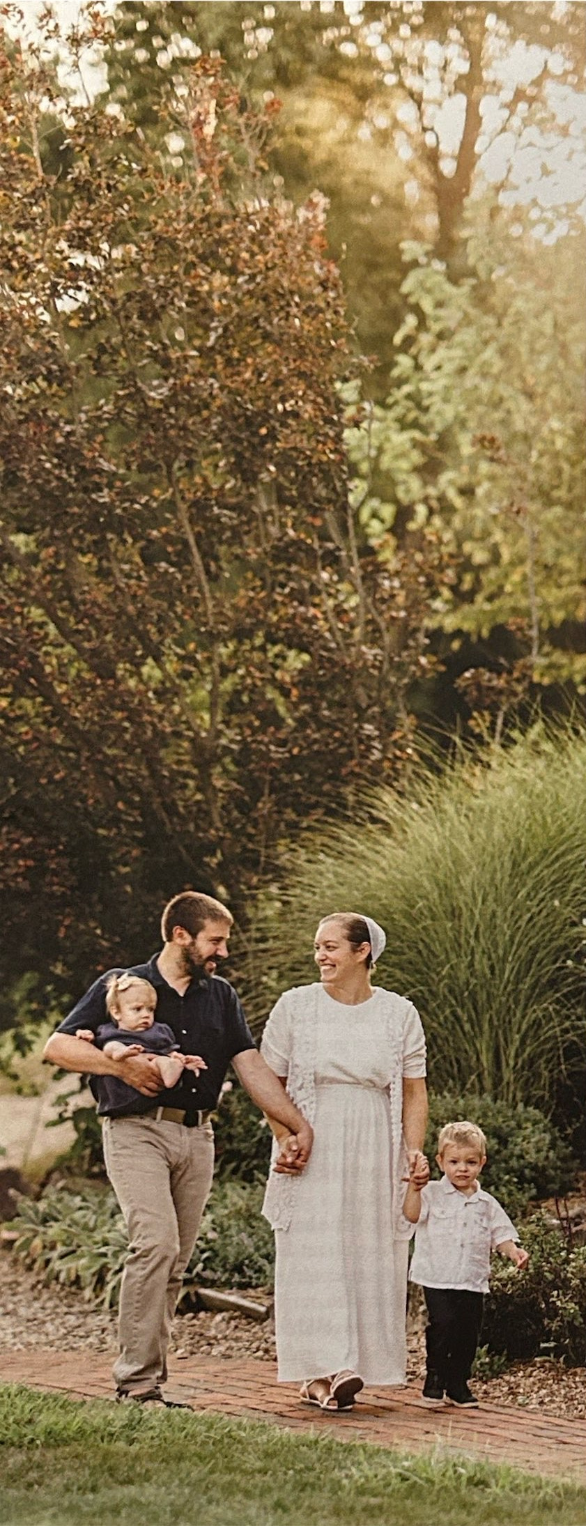 Parents walk along a garden path with two young children.