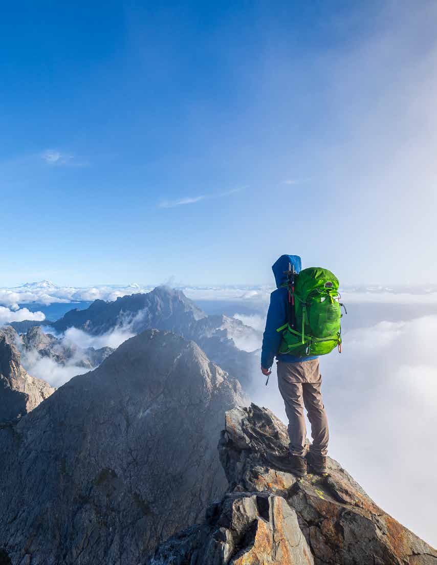 A hiker with a bright green backpack standing on a mountain summit above clouds