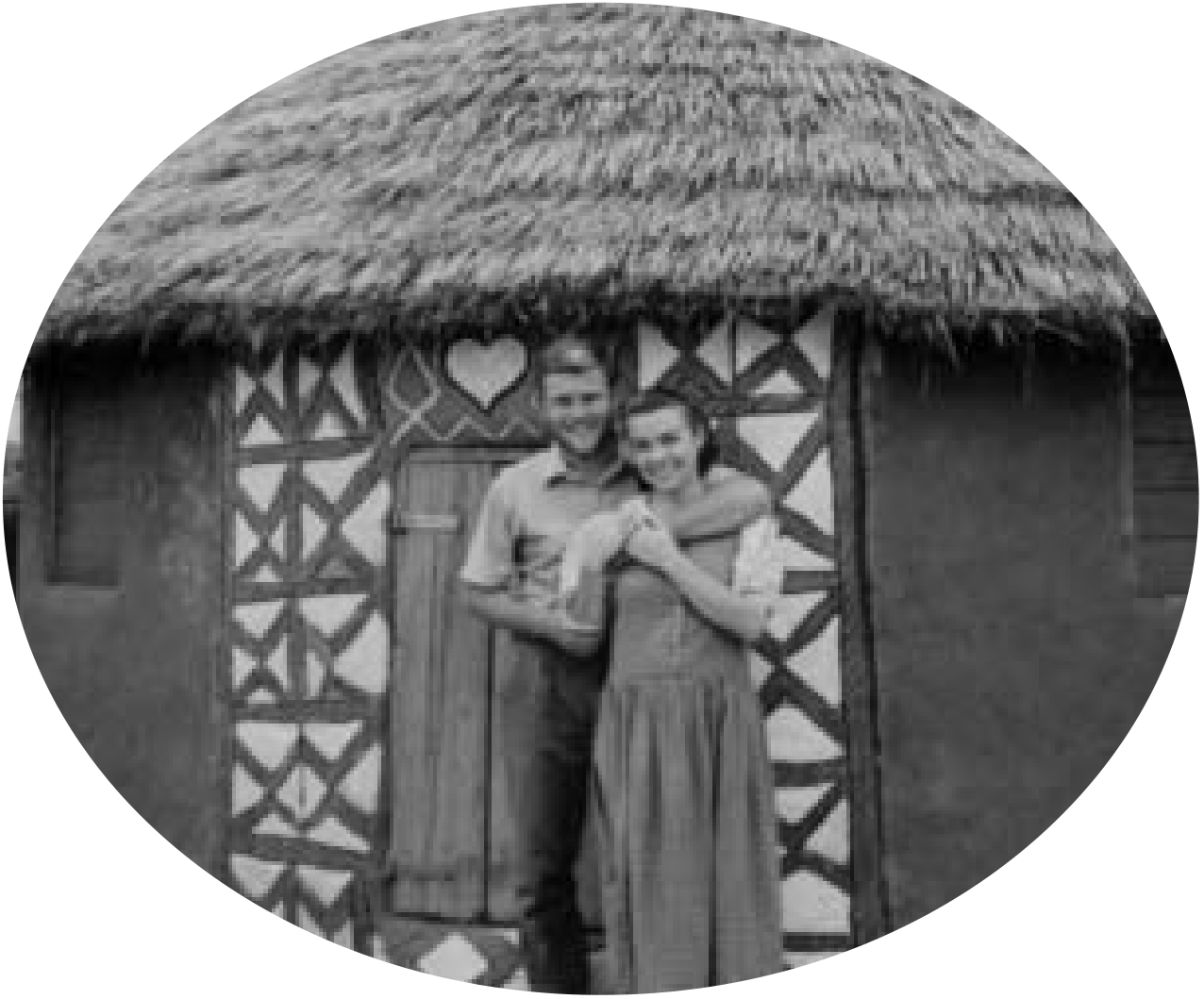 A couple standing outside a thatched building.