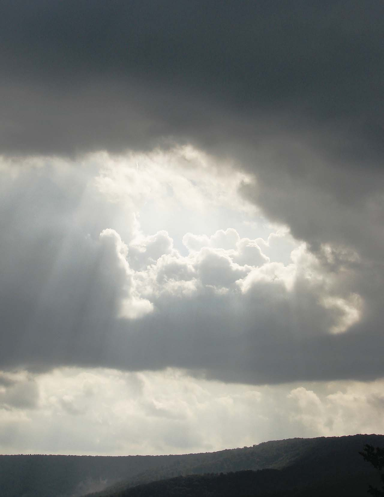 Sunbeams breaking through a cloudy sky above dark hills