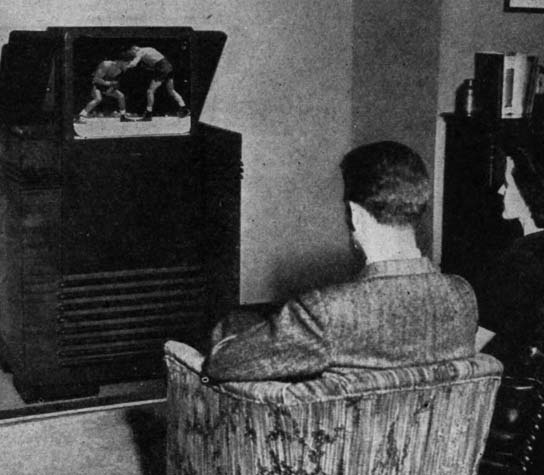 A man seated in a chair watching television