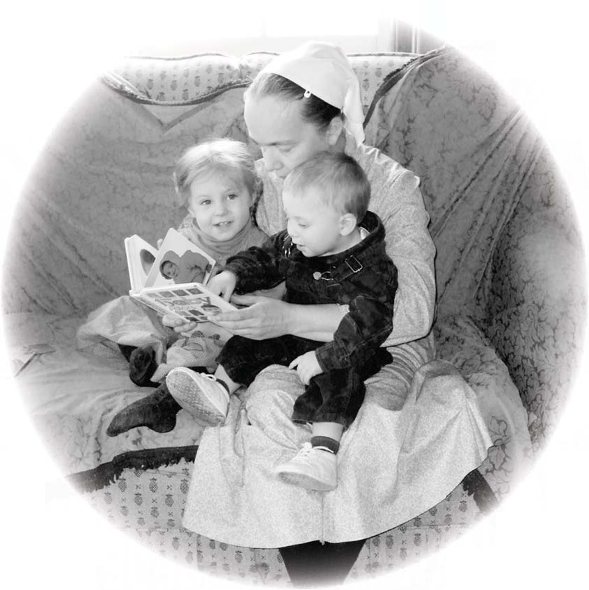 Mary sits with Jeanna and Brendan, looking at a picture book on a sofa