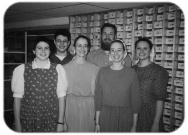 Six people standing together in a room lined with cassette boxes