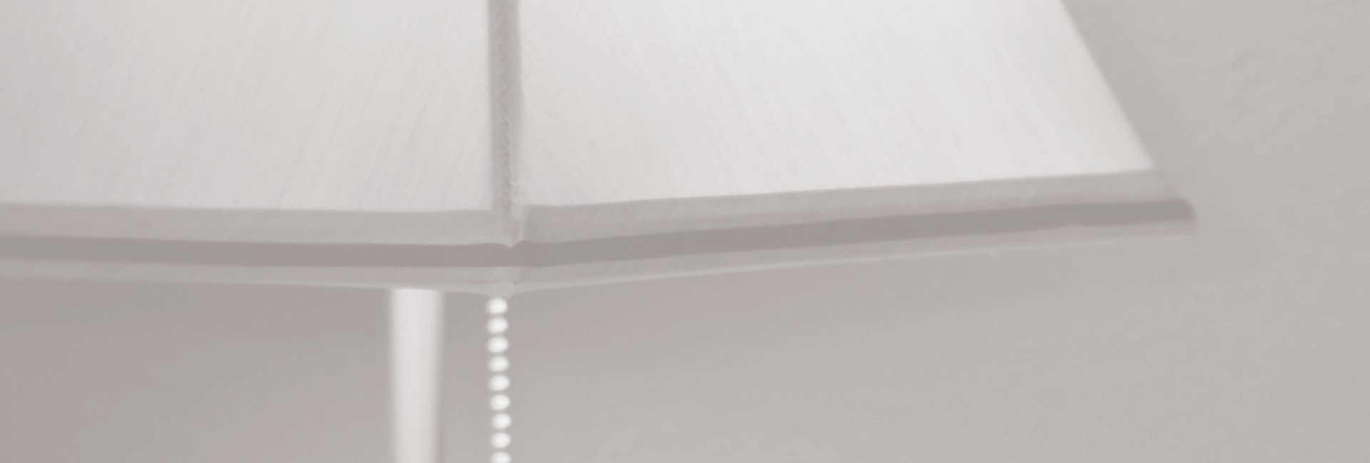 A lampshade and pull chain before a softly lit window