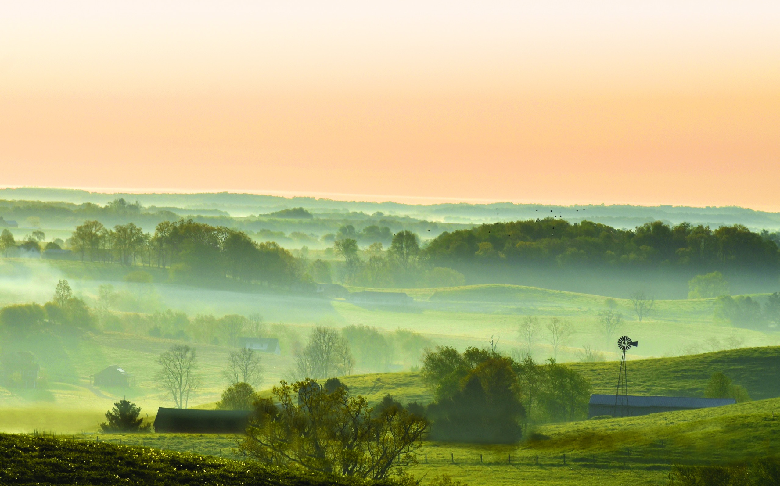 Sunrise over misty green hills, farms, and a windmill