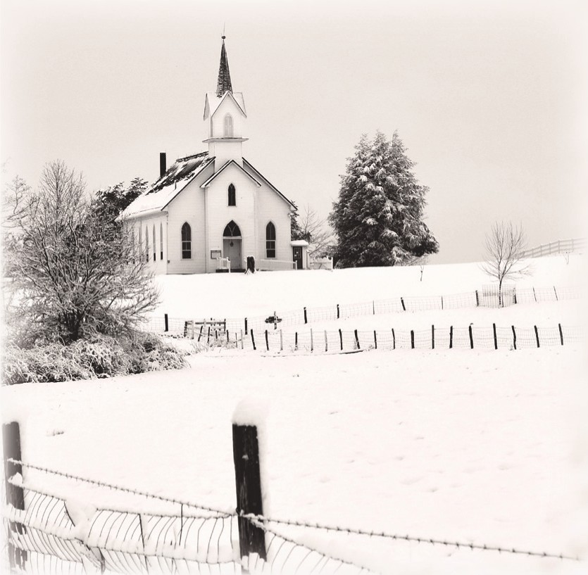 A snow-covered country church behind a wooden fence
