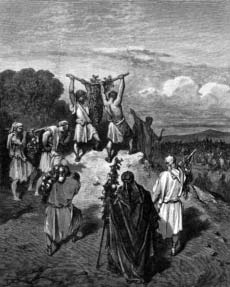 Two men carry a large cluster of grapes on a pole above a gathering of people.