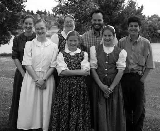 Seven people standing outdoors in front of trees.