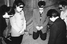 People kneeling together, with black bars covering their eyes in the source photograph