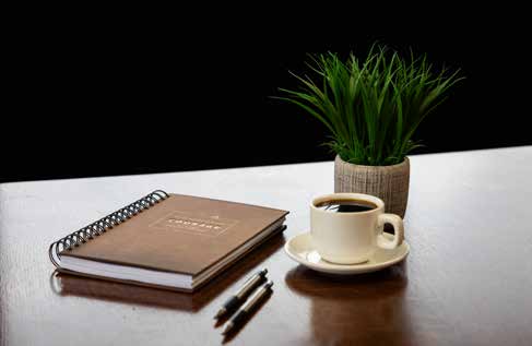 A notebook, pens, coffee, and a plant on a desk