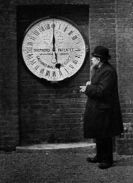 A man standing beside a large wall clock