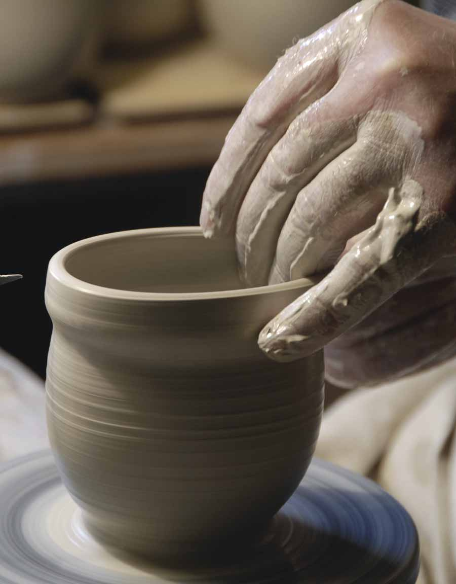 A potter’s hand shapes a clay vessel on a wheel