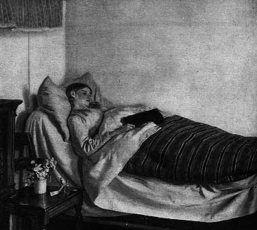 A person lies in bed under a striped blanket.